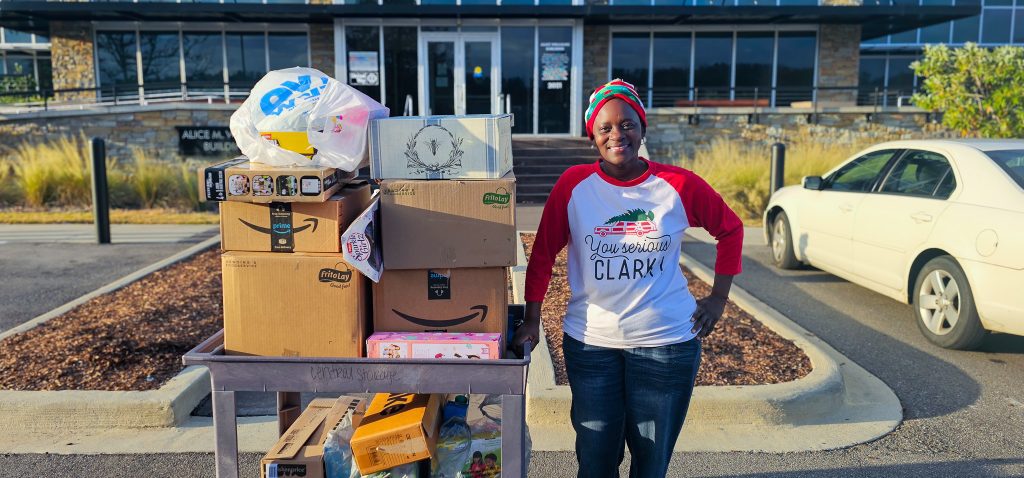 Volunteer standing beside a cart loaded with boxes and bags of donated toys outside a building during the Publix Holiday Toy Drive in partnership with United Way.