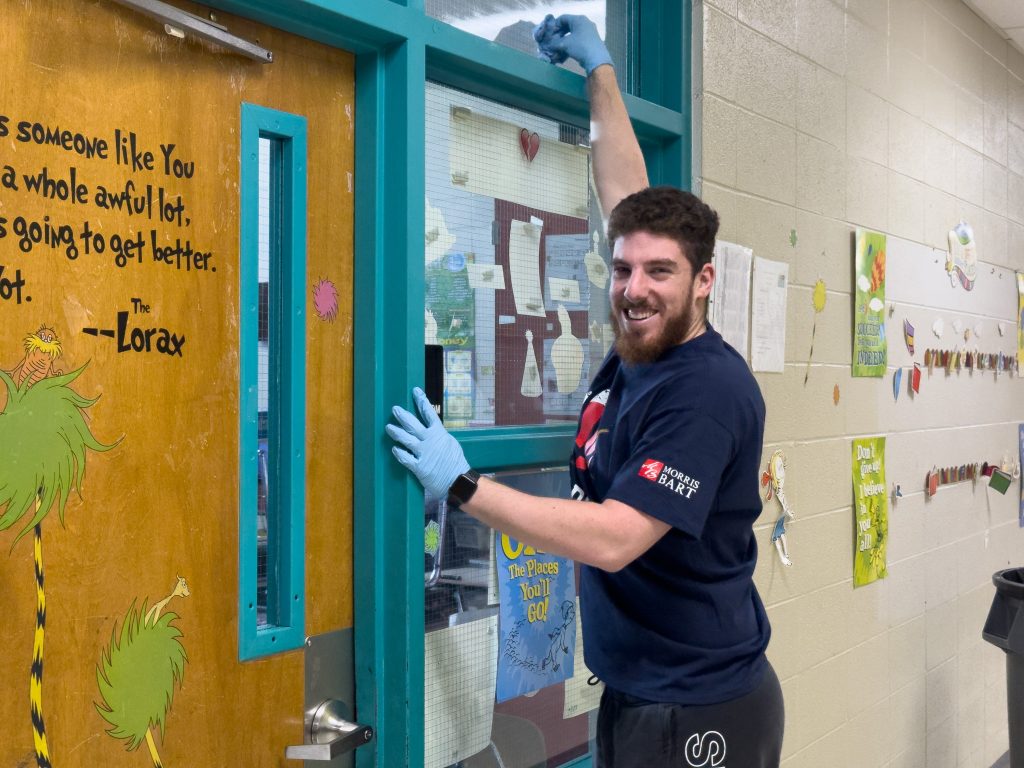 A smiling volunteer cleans an elementary school classroom window at a United Way Hands On Back-to-School Beautification Volunteer Day.