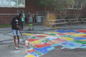 Young volunteer pressure washes painting of United States on Avondale Elementary School playground pavement